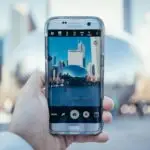 Hand holding smartphone capturing Cloud Gate reflection in Chicago skyline.