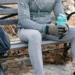 A man in activewear rests on a park bench holding a shake bottle, enjoying a break.
