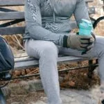 A man in activewear rests on a park bench holding a shake bottle, enjoying a break.