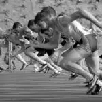 Athletes burst from the blocks during a sprint race, captured in monochrome.