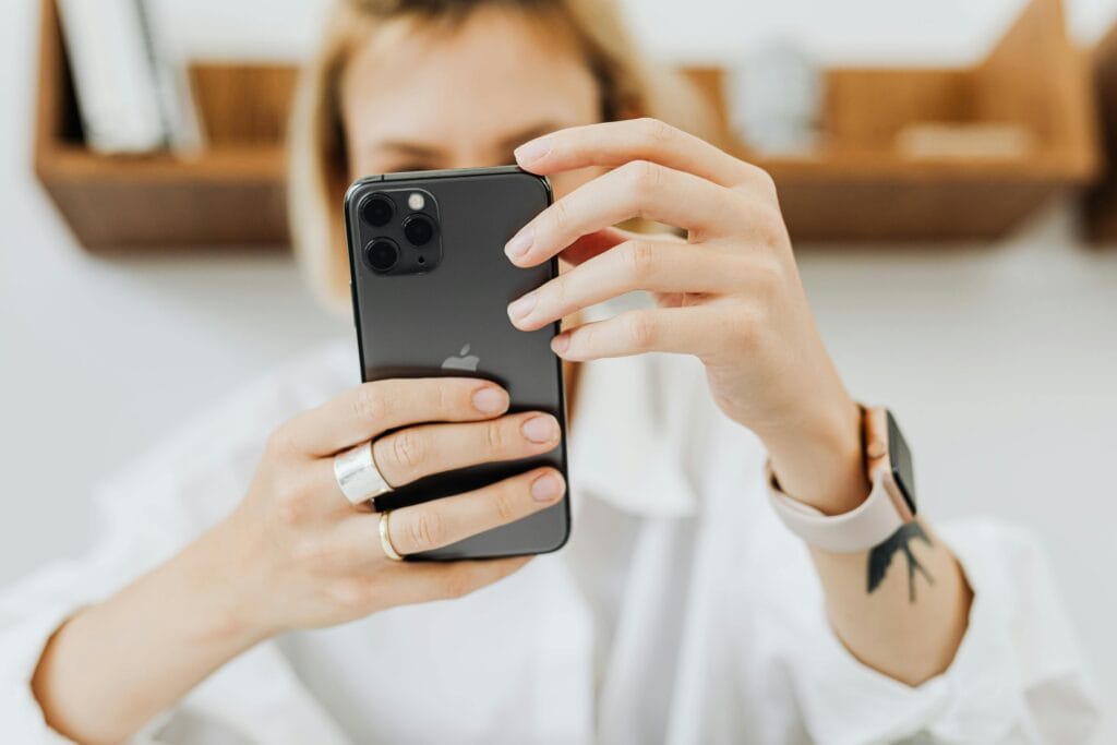 A close-up image of a woman holding a smartphone, indoors. Focus on hands and electronic device.