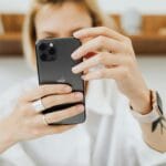 A close-up image of a woman holding a smartphone, indoors. Focus on hands and electronic device.