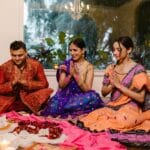 Family celebrating Diwali with prayer, candles, and traditional clothing indoors.