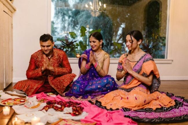 Family celebrating Diwali with prayer, candles, and traditional clothing indoors.
