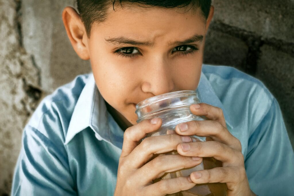 Close-up of a boy drinking from a glass jar outdoors in Cabo San Lucas, Mexico.