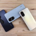 Minimalist flat lay of three smartphones on a wooden surface, showcasing sleek design and camera features.