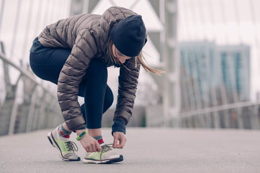 Woman in activewear tying running shoes on a city bridge, ready for a winter jog.
