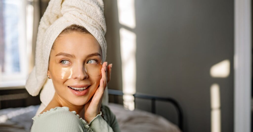 A woman with a towel wrapped around her head applying under-eye masks in a sunlit room.